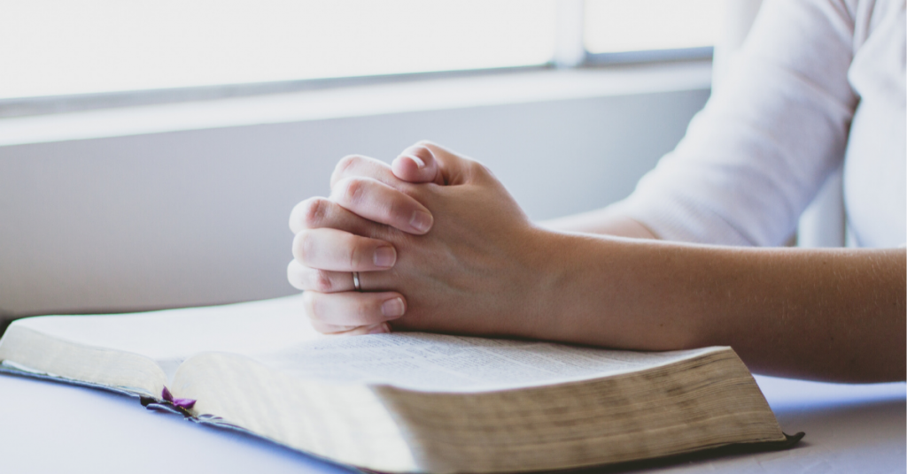Hands praying on bible